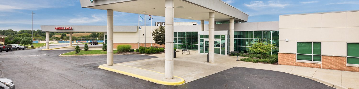 Image of a medical building with a sign that reads "Ephraim McDowell Fort Logan Hospital" and a small green sign to the right that reads "ER" on a sunny day.