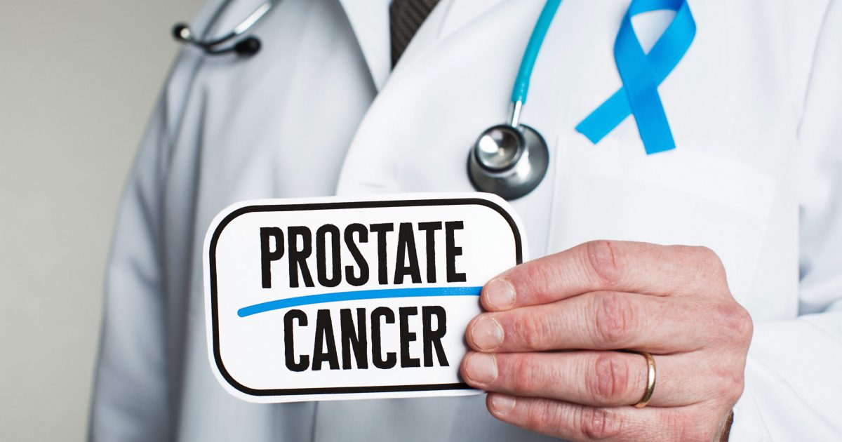Doctor with stethoscope in white lab coat holding sign reading prostate cancer